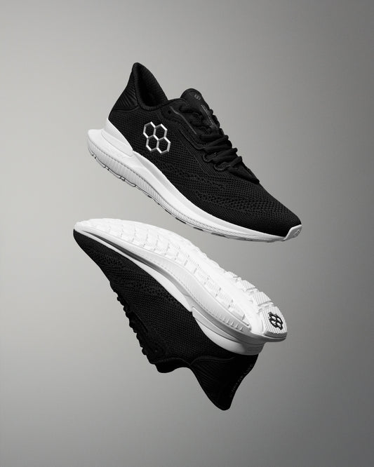 Black running shoes with white soles on a gray background