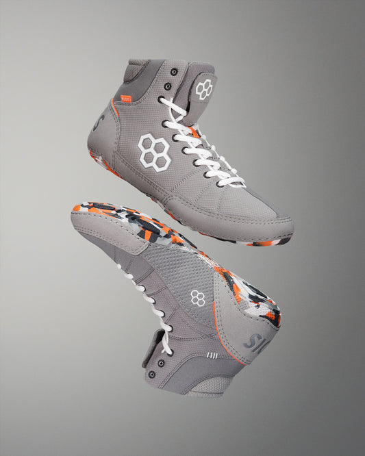 High-top athletic shoes feature a gray upper with vibrant orange and black accents, designed for style and support, showcased against a soft gradient background.