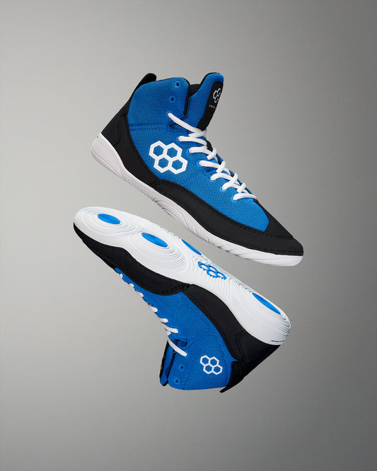 Blue Wrestling shoes feature a vibrant blue upper and black paneling, with white accents and a focus on traction, set against a neutral gray backdrop.