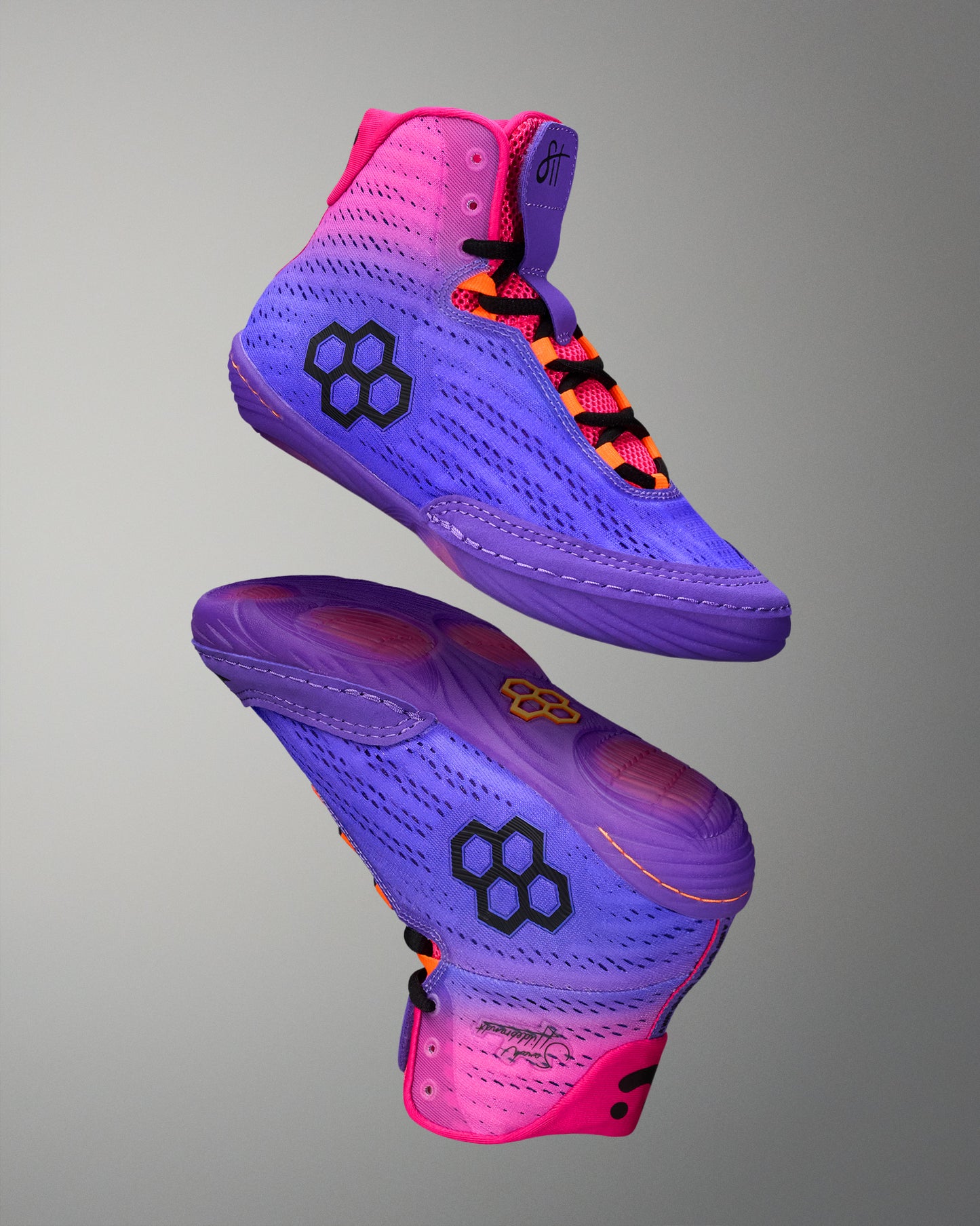 Purple and pink wrestling shoes with a brand logo on a gray background
