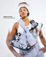 A woman in a light gray athletic outfit holds up a black and white patterned sneaker, with a second identical sneaker blurred in front of her. Text on the left reads 'KENNEDY BLADES OLYMPIC SILVER MEDALIST'.