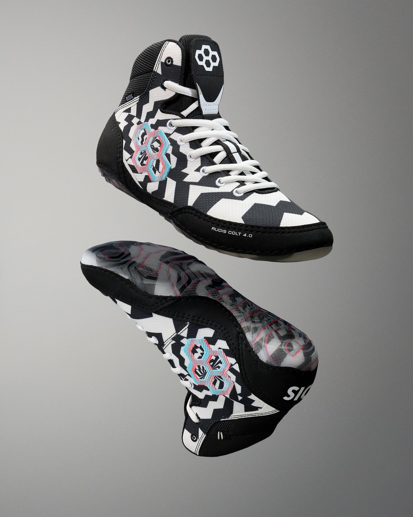 A pair of high-top athletic wrestling shoes shown from the front and side against a neutral gray gradient background. The shoes feature a black, white, and gray geometric pattern with pink and light blue graphic accents on the sides and a white flower logo on the tongue.