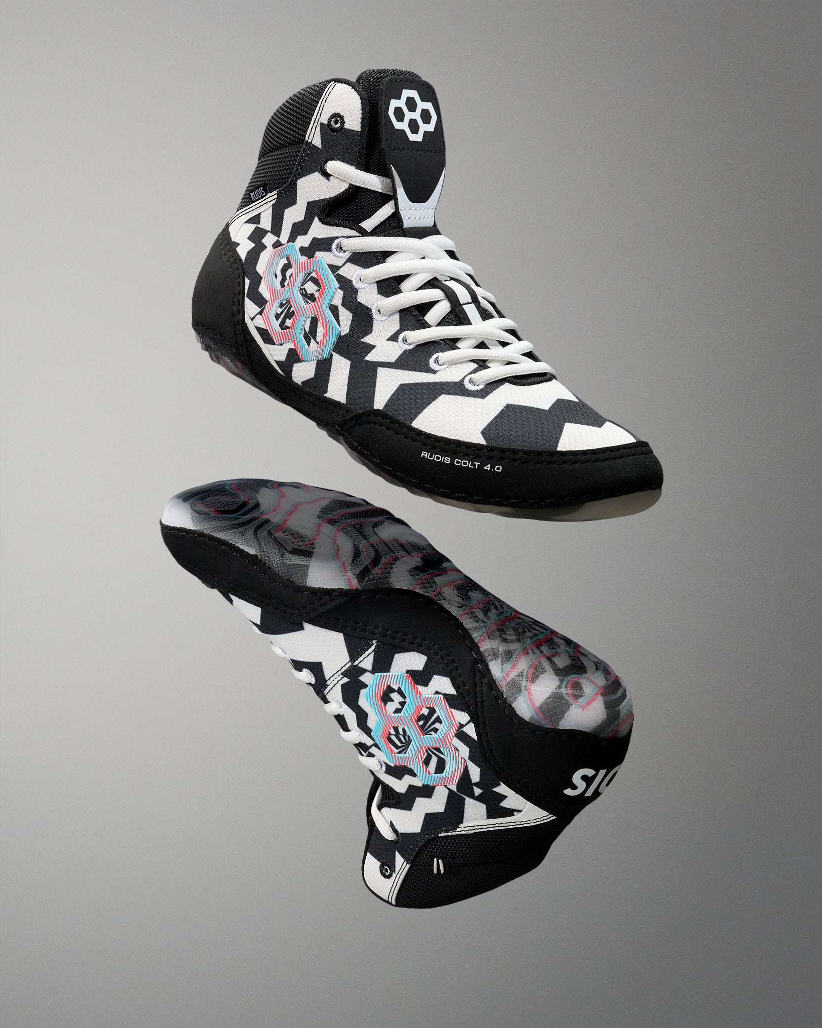 A pair of high-top athletic wrestling shoes shown from the front and side against a neutral gray gradient background. The shoes feature a black, white, and gray geometric pattern with pink and light blue graphic accents on the sides and a white flower logo on the tongue.