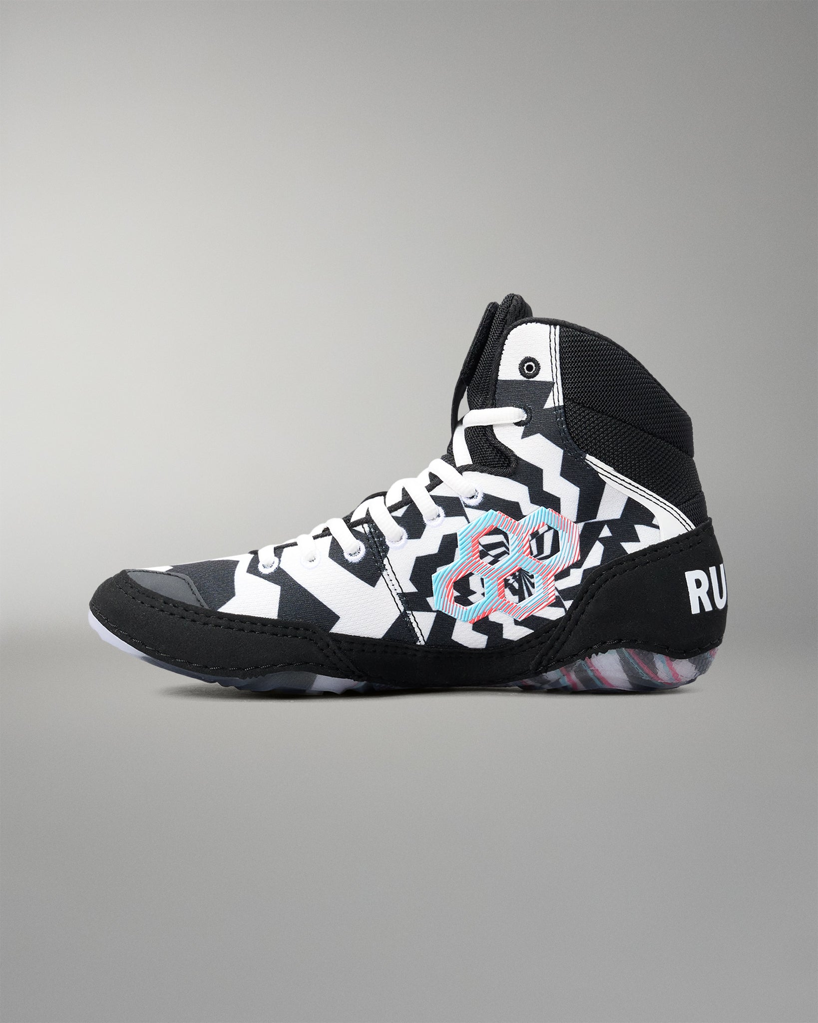 A high-top athletic wrestling shoe in black, white, and gray, featuring a bold geometric pattern and a central circular graphic with pink, blue, and red accents. The brand name 'RUDIS' is visible on the heel.
