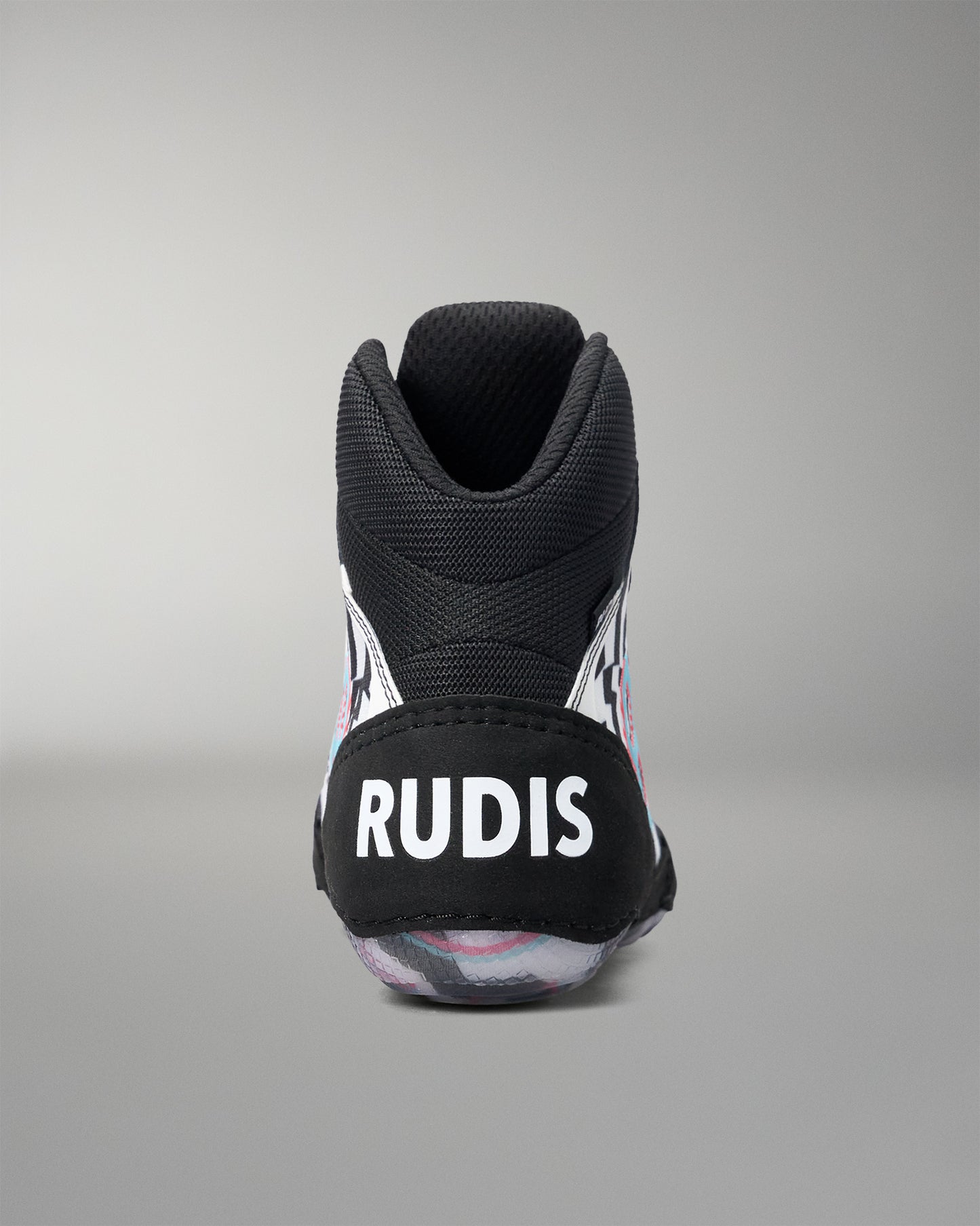A black high-top athletic wrestling shoe shown from the back, featuring a black heel counter with the white text 'RUDIS' and a patterned sole with pink, white, and gray details, set against a neutral gray background.