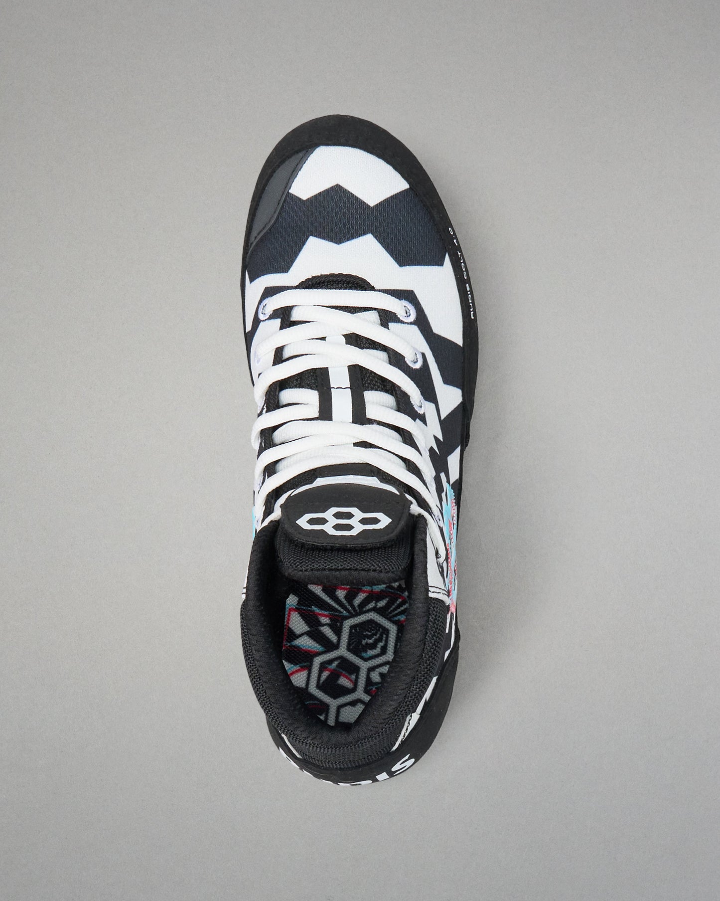 A single athletic wrestling shoe shown from a top-down view on a neutral gray background. The shoe features a black and white geometric pattern with white laces and a black tongue displaying a white logo.