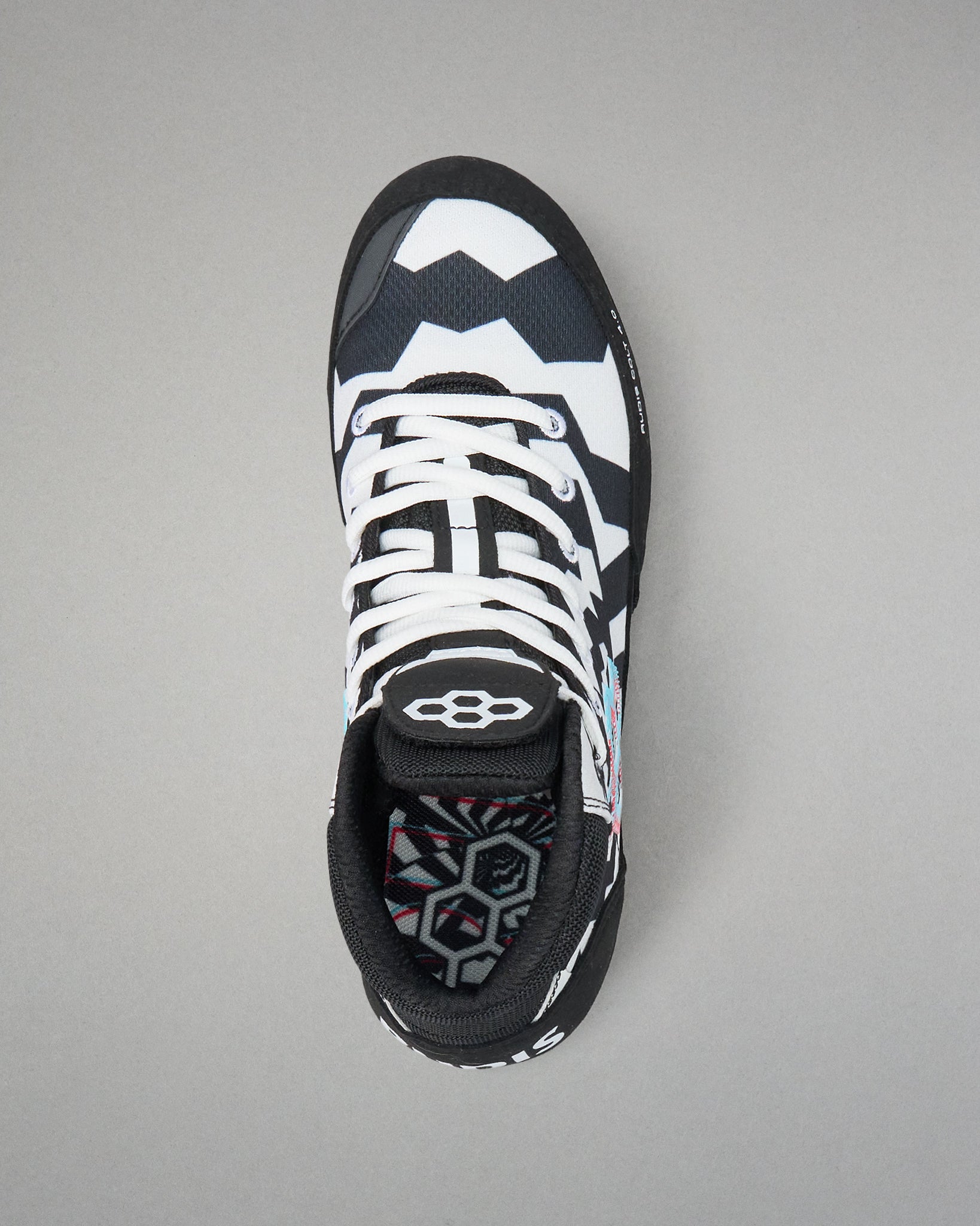 A single athletic wrestling shoe shown from a top-down view on a neutral gray background. The shoe features a black and white geometric pattern with white laces and a black tongue displaying a white logo.