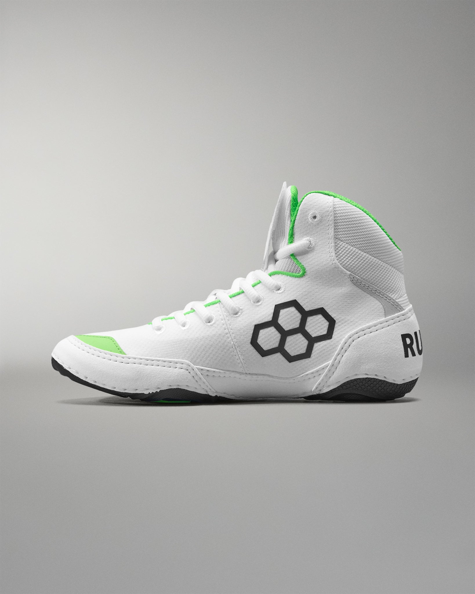 White wrestling shoes with green accents and a black logo on a gray background