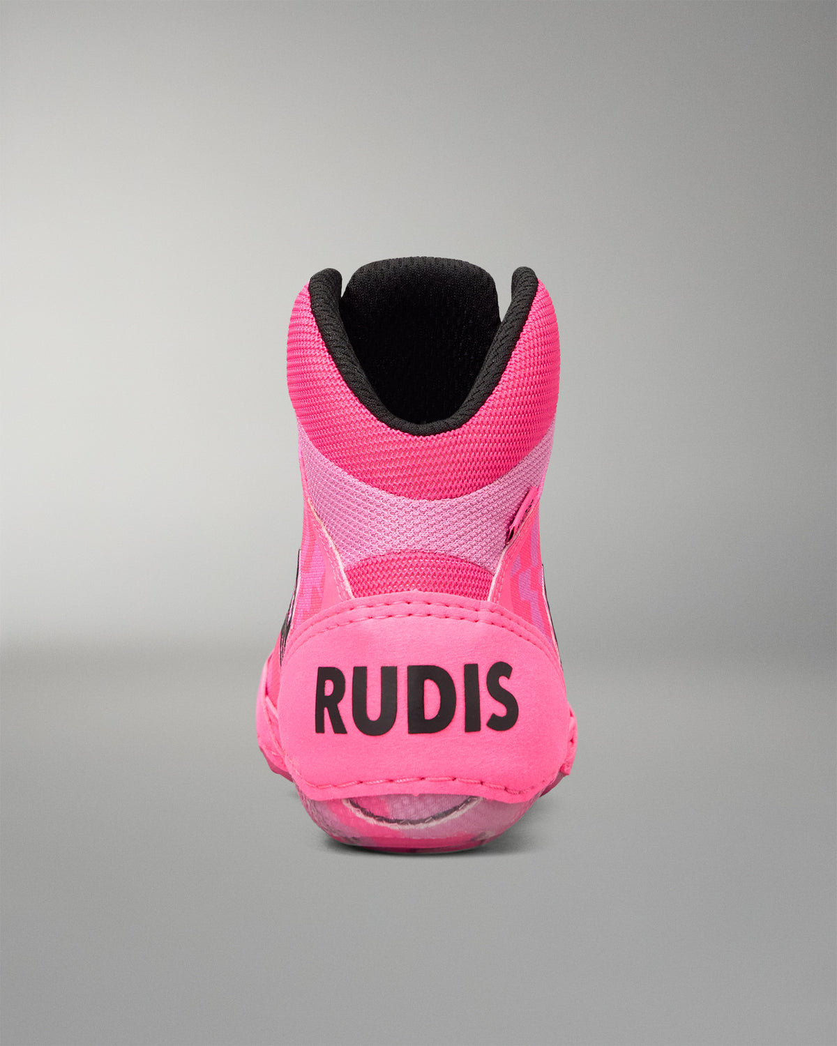 A bright pink high-top Wrestling shoe shown from the back, featuring the brand name 'RUDIS' in black text on the heel, a black collar lining, and a translucent pink sole, set against a neutral gray background.