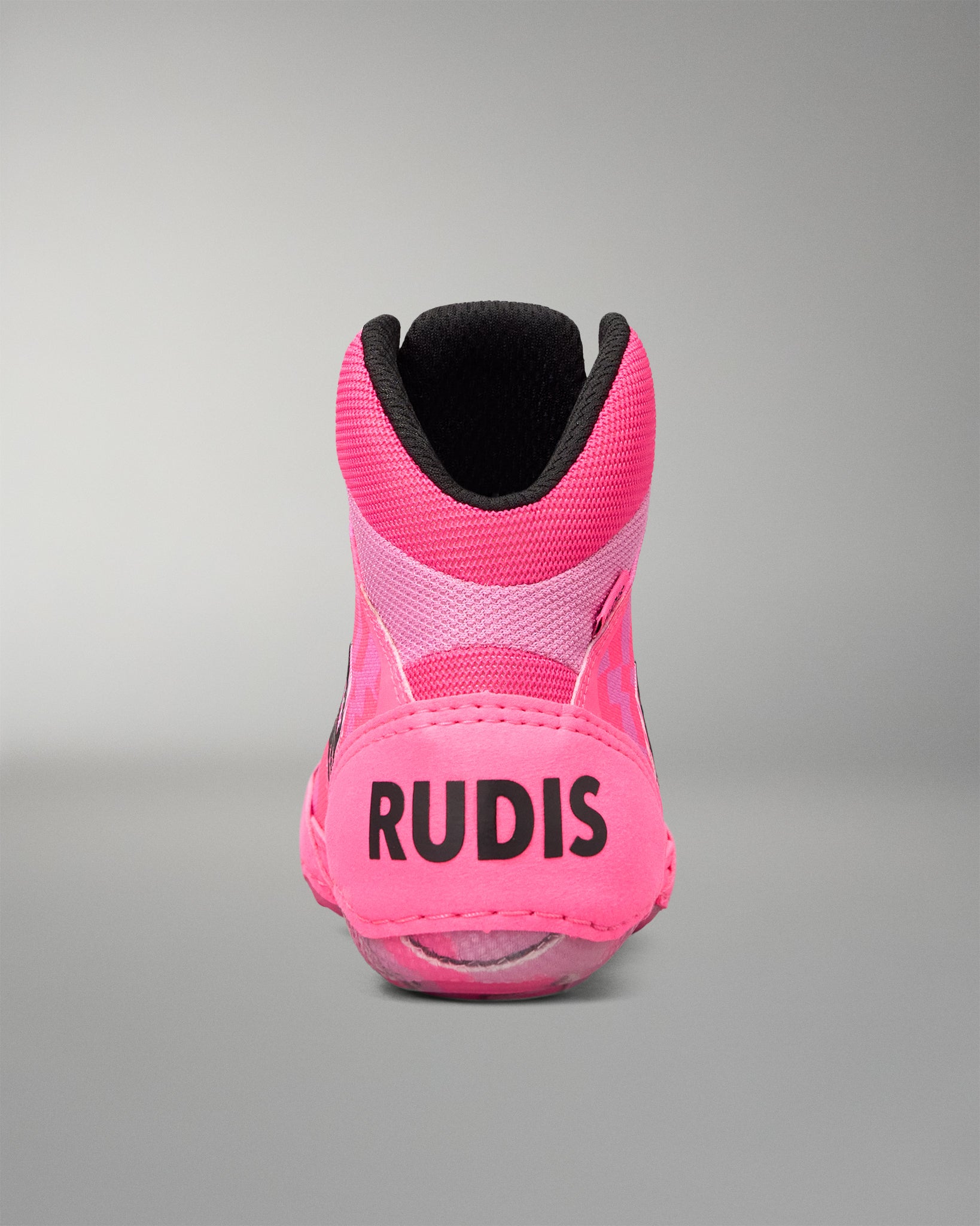 A bright pink high-top Wrestling shoe shown from the back, featuring the brand name 'RUDIS' in black text on the heel, a black collar lining, and a translucent pink sole, set against a neutral gray background.