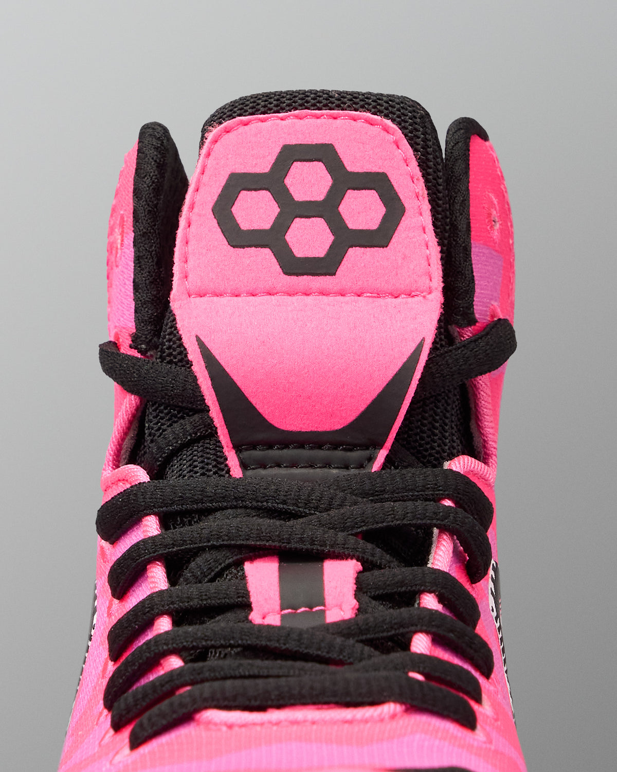 Close-up of the top of a high-top Wrestling shoe in bright pink and black, showing the tongue with a black geometric logo, black laces, and black mesh around the collar on a gray background.