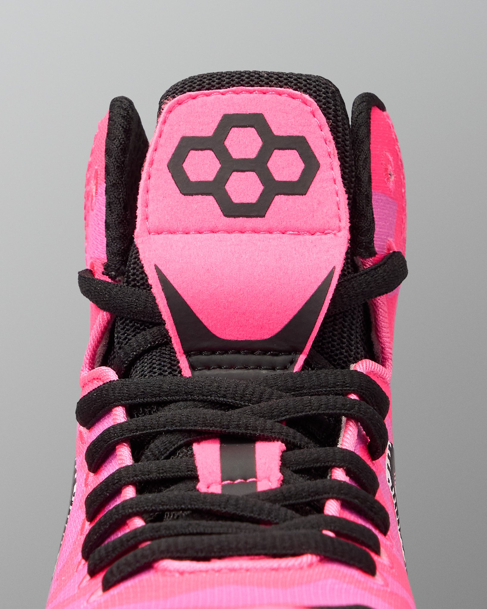 Close-up of the top of a high-top Wrestling shoe in bright pink and black, showing the tongue with a black geometric logo, black laces, and black mesh around the collar on a gray background.