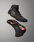 A pair of high-top Wrestling shoes shown floating against a neutral gray gradient background, displaying both the black upper with gray hexagonal accents and the black sole with a vibrant orange and gray camouflage pattern.