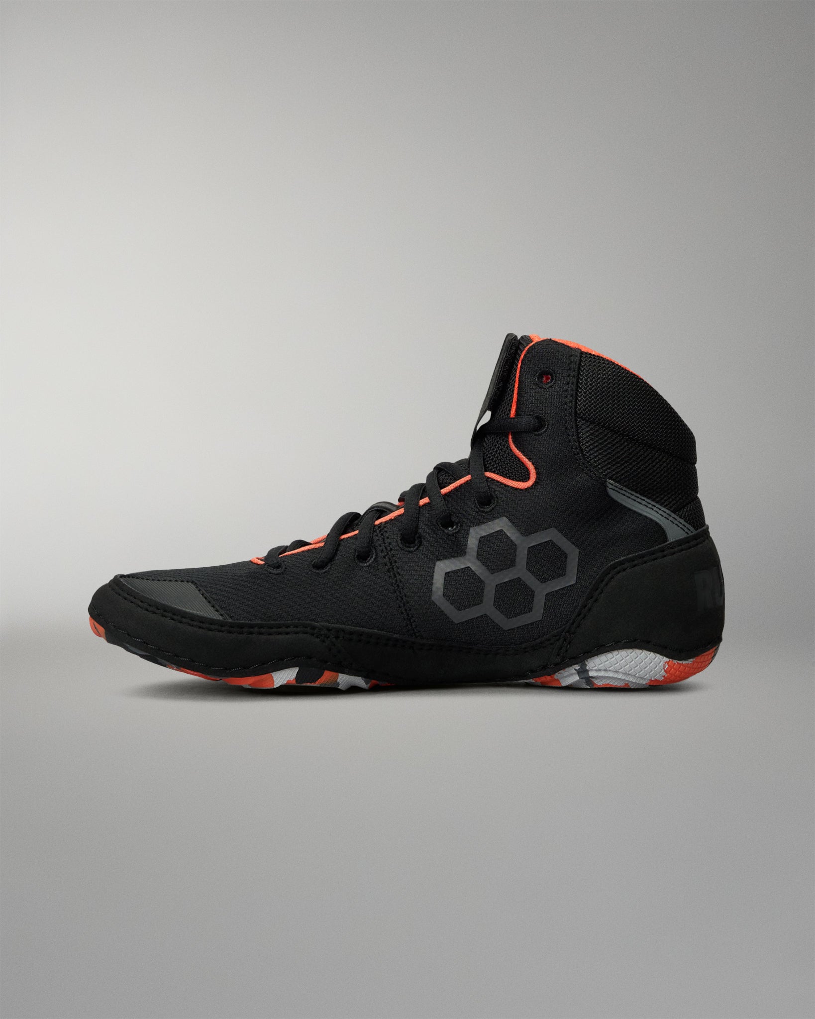 A high-top Wrestling shoe in black with gray hexagonal side detailing and bright orange accents on the collar, laces, and outsole, shown against a neutral gray background.