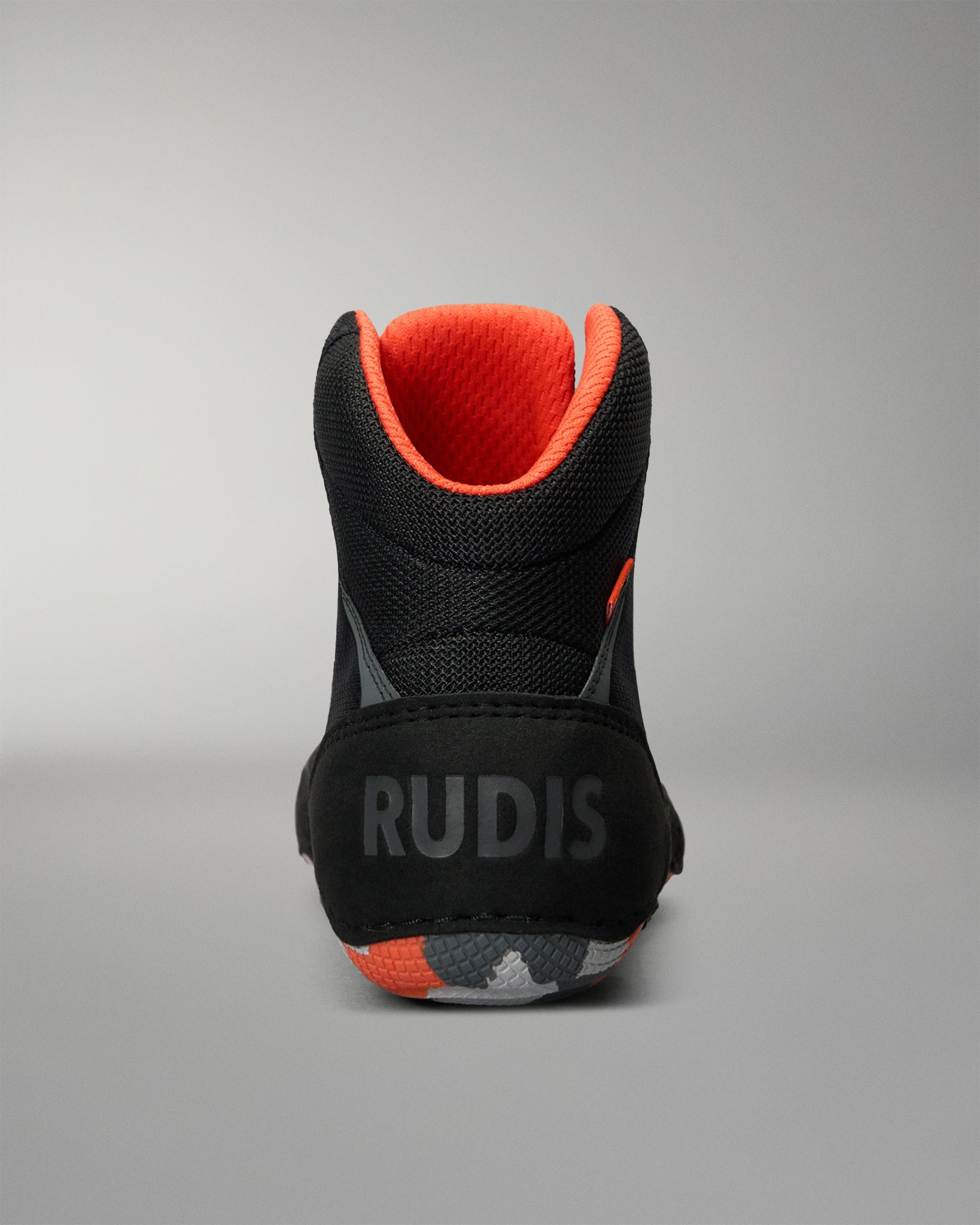 A single high-top Wrestling shoe shown from the back on a neutral gray background. The shoe is primarily black with a bright orange interior lining and a gray 'RUDIS' logo printed on the heel.