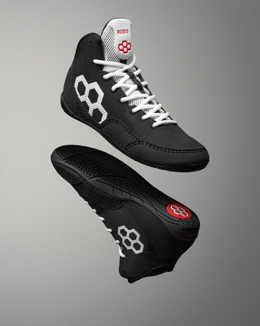 A pair of black athletic high-top wrestling shoes shown from the side and sole views against a gray gradient background. The shoes feature white laces, white geometric side logos, and a red logo on the tongue and heel.