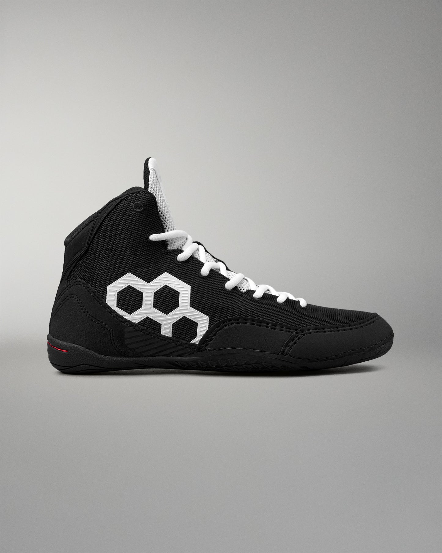 A black high-top wrestling shoe with white laces and a prominent white geometric hexagon logo on the side, shown against a neutral gray background.