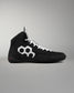 A black high-top wrestling shoe with white laces and a prominent white geometric hexagon logo on the side, shown against a neutral gray background.