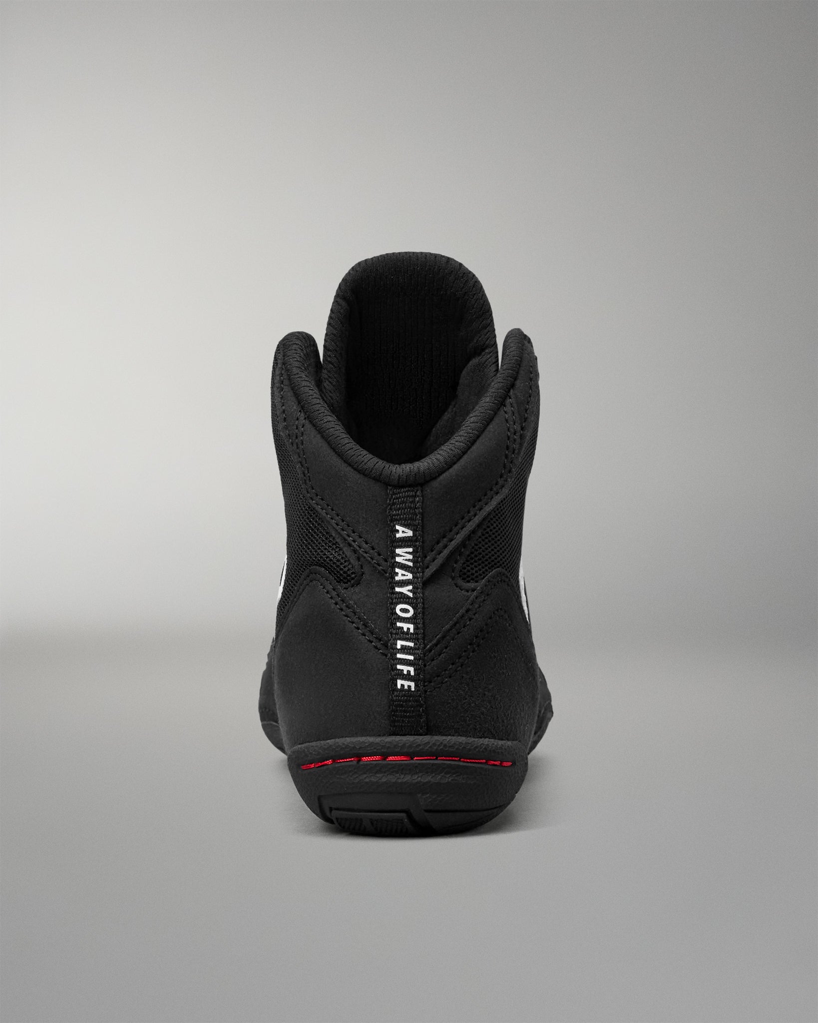 A black high-top wrestling shoes shown from the back, featuring a black collar, white vertical text reading 'A WAY OF LIFE' on the heel, and a thin red line of stitching around the midsole.