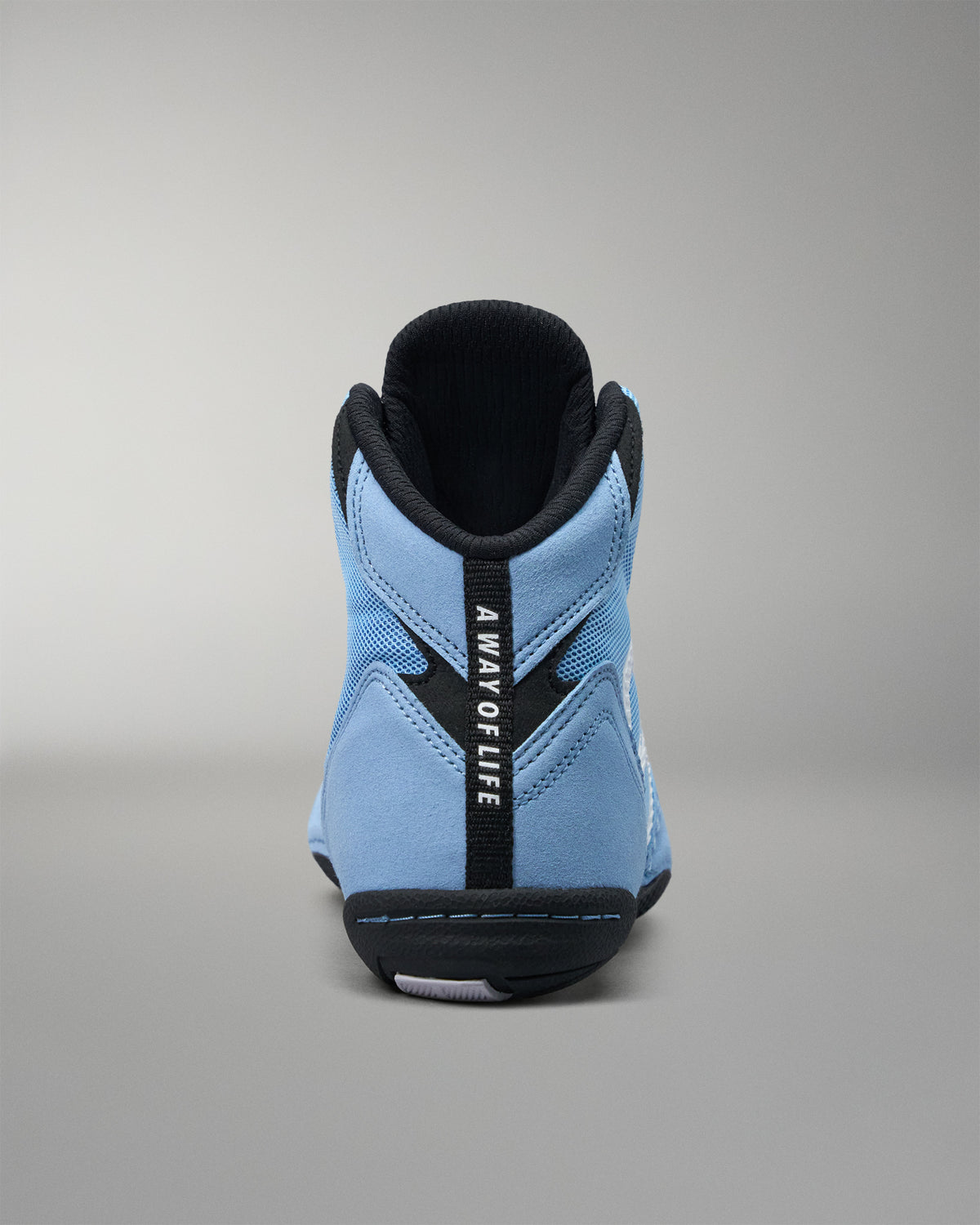 A light blue high-top wrestling shoe shown from the back, featuring a black heel counter, black collar, and a vertical black strap with the text 'A WAY OF LIFE'.