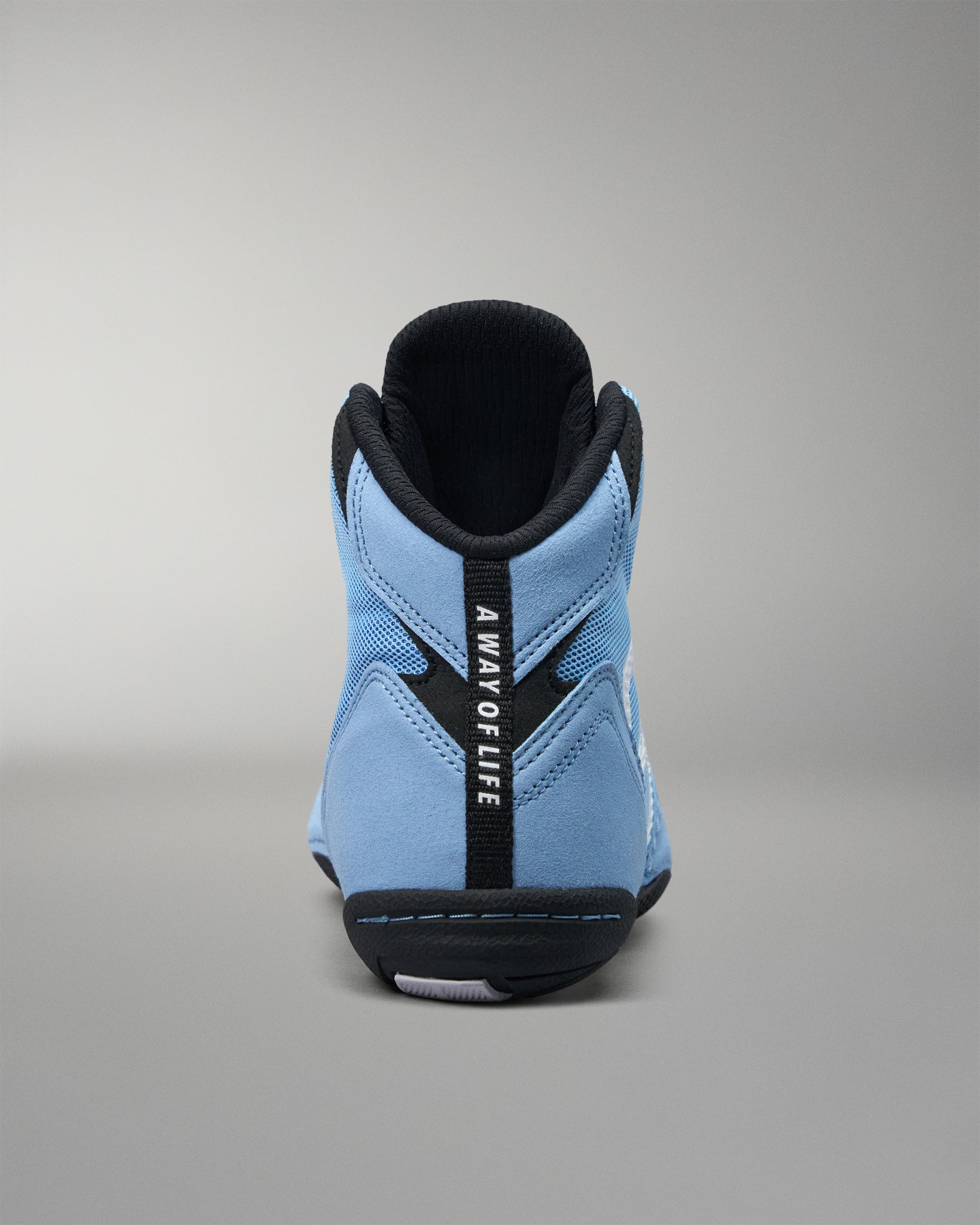 A light blue high-top wrestling shoe shown from the back, featuring a black heel counter, black collar, and a vertical black strap with the text 'A WAY OF LIFE'.