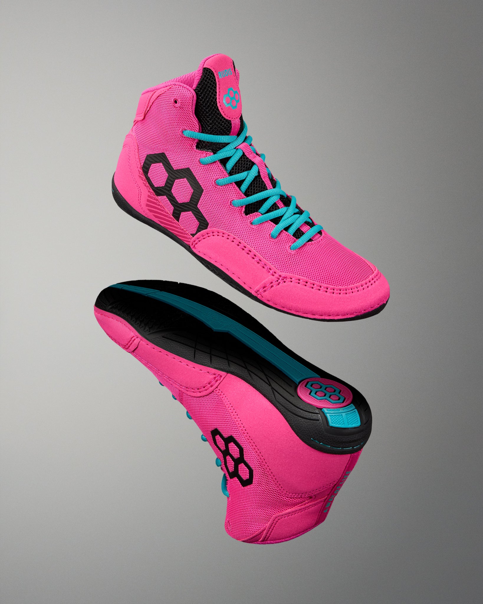 A pair of high-top athletic wrestling shoes in bright pink, shown from the side and sole views against a neutral gray gradient background. The shoes feature black geometric side logos, turquoise laces, and a black and turquoise outsole.