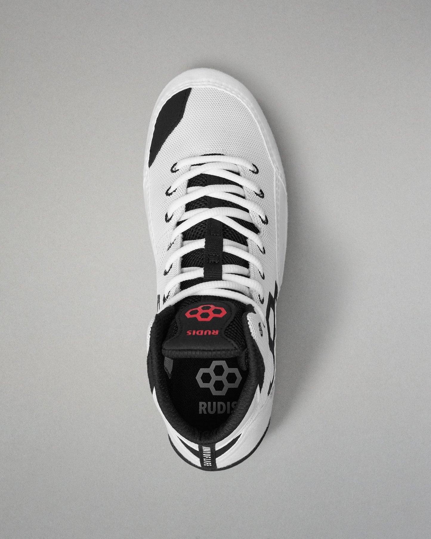 A single white and black wrestling shoe shown from a top-down view on a neutral gray background. The shoe features a white upper with black accents, white laces, and a black heel counter with a red logo and the brand name 'RUDIS'.