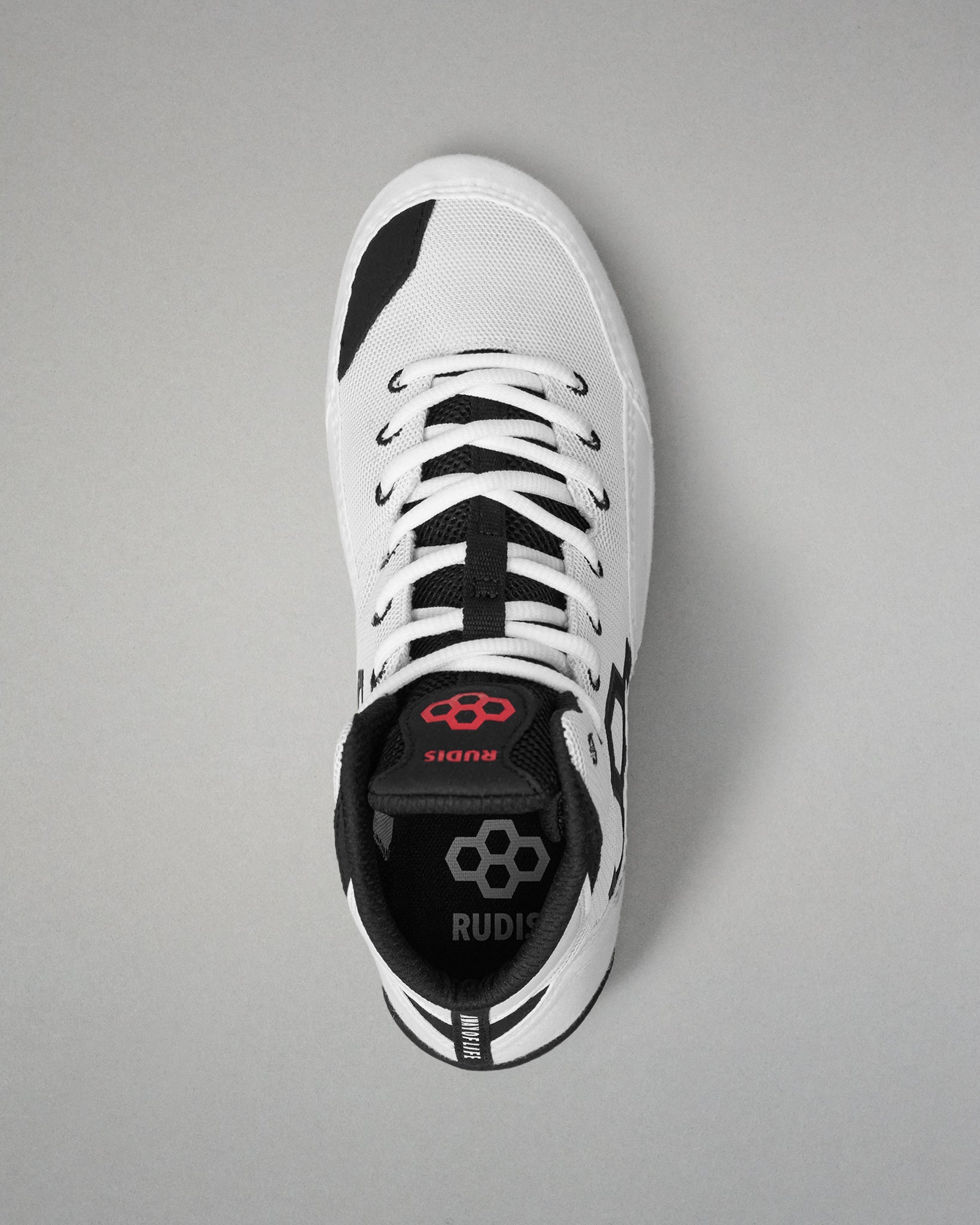 A single white and black wrestling shoe shown from a top-down view on a neutral gray background. The shoe features a white upper with black accents, white laces, and a black heel counter with a red logo and the brand name 'RUDIS'.