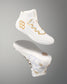 A pair of white wrestling shoes with gold quadhex and wavy geometric logo details, shown floating against a neutral gray gradient background.