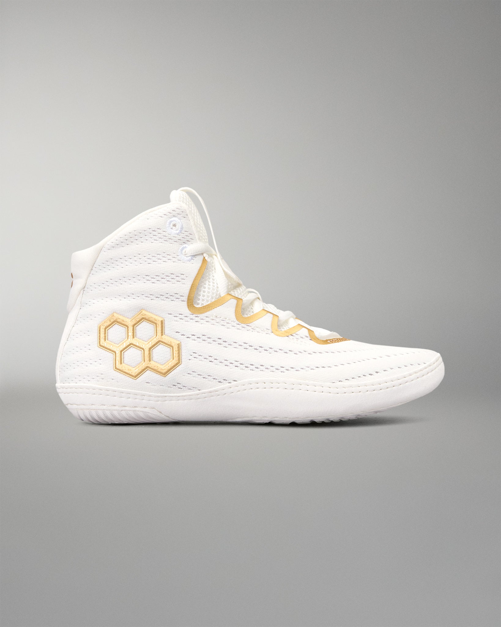 A white wrestling shoes with gold accents, featuring a gold quadhex logo on the side and gold embroidered details around the eyelets, shown against a neutral gray background.