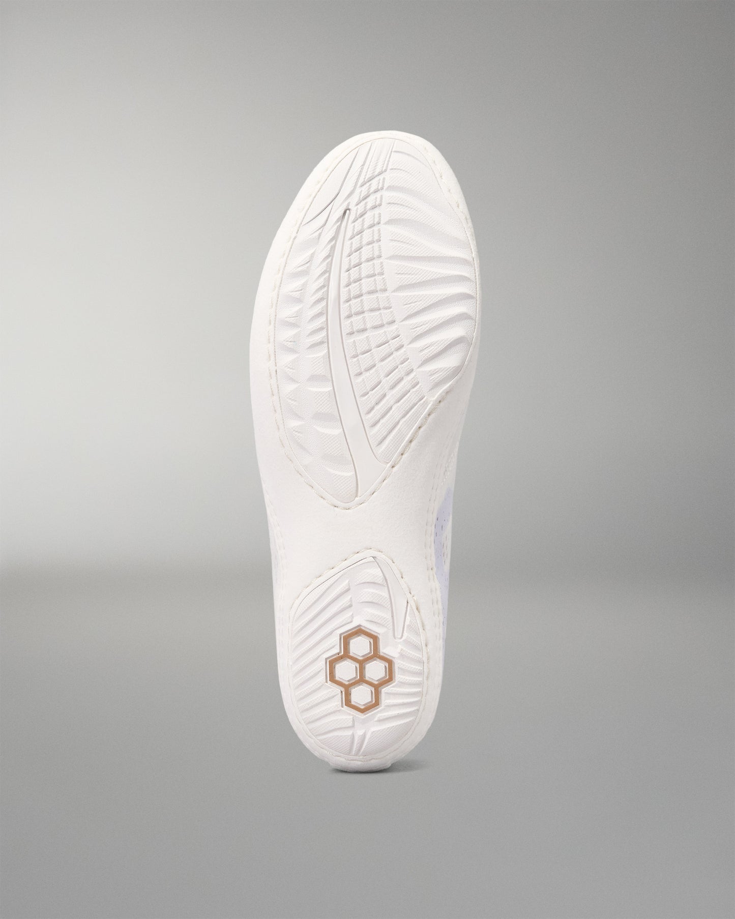The white outsole of a wrestling shoe, showing textured tread patterns and a small gold geometric logo near the heel, set against a neutral gray background.