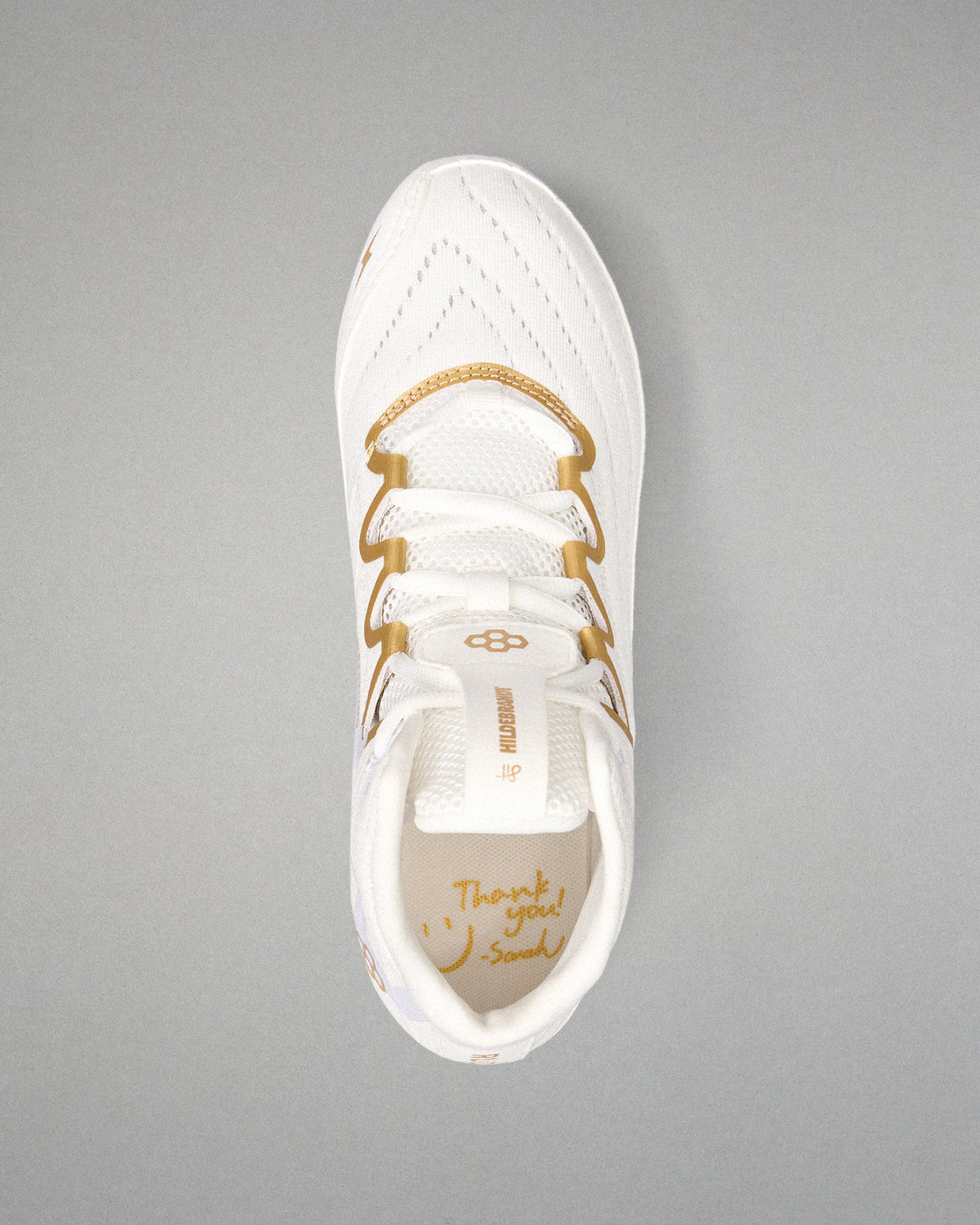 A white wrestling shoe with gold accents, including the laces and branding, shown from a top-down view on a neutral gray background.