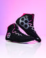 A pair of black high-top wrestling shoes with vibrant pink and gray accents, displayed on a reflective white surface against a pink gradient background.