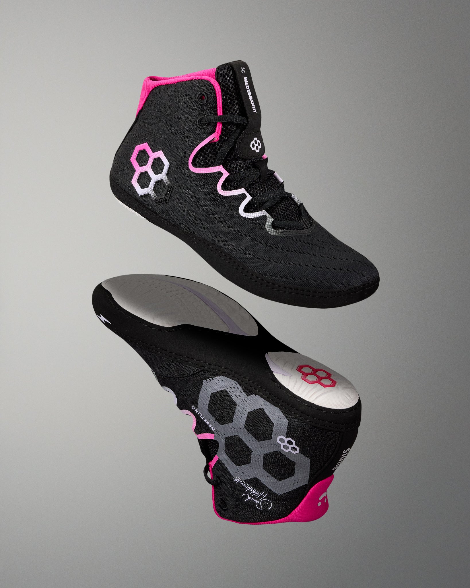 A pair of black high-top wrestling shoes with bright pink and silver accents, shown from the side and sole views against a neutral gray background.