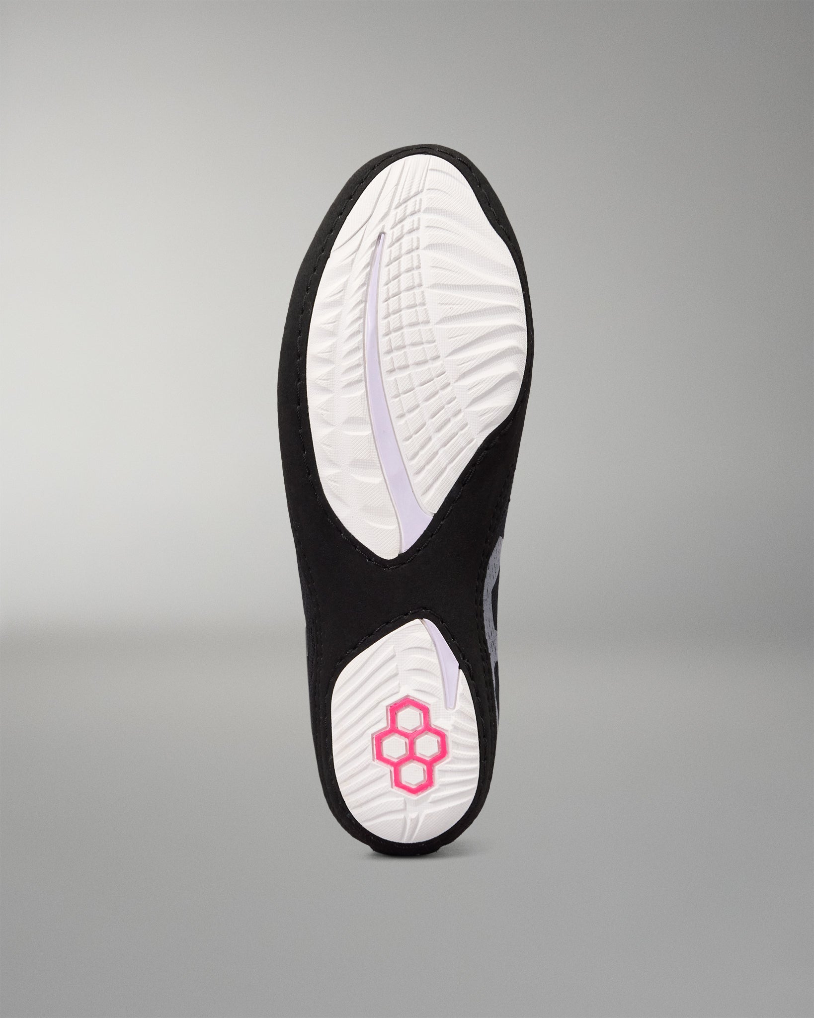 The outsole of a black and white athletic wrestling shoe, showing a textured white tread pattern with a pink geometric logo near the heel, set against a neutral gray background.