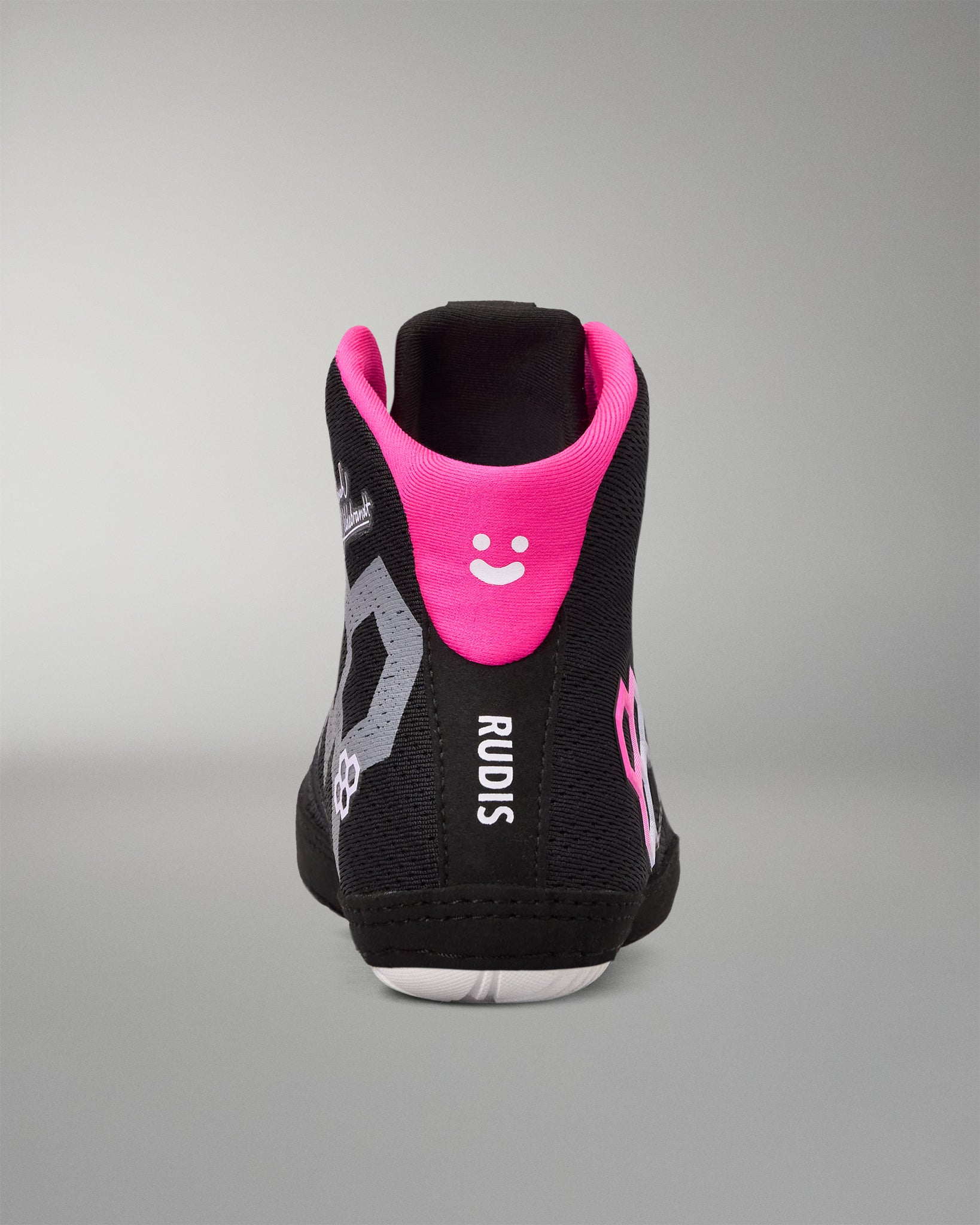 A high-top black wrestling shoe shown from the back, featuring a vibrant hot pink collar lining with a white smiley face, gray graphic accents, and the brand name 'RUDIS' printed vertically in white.