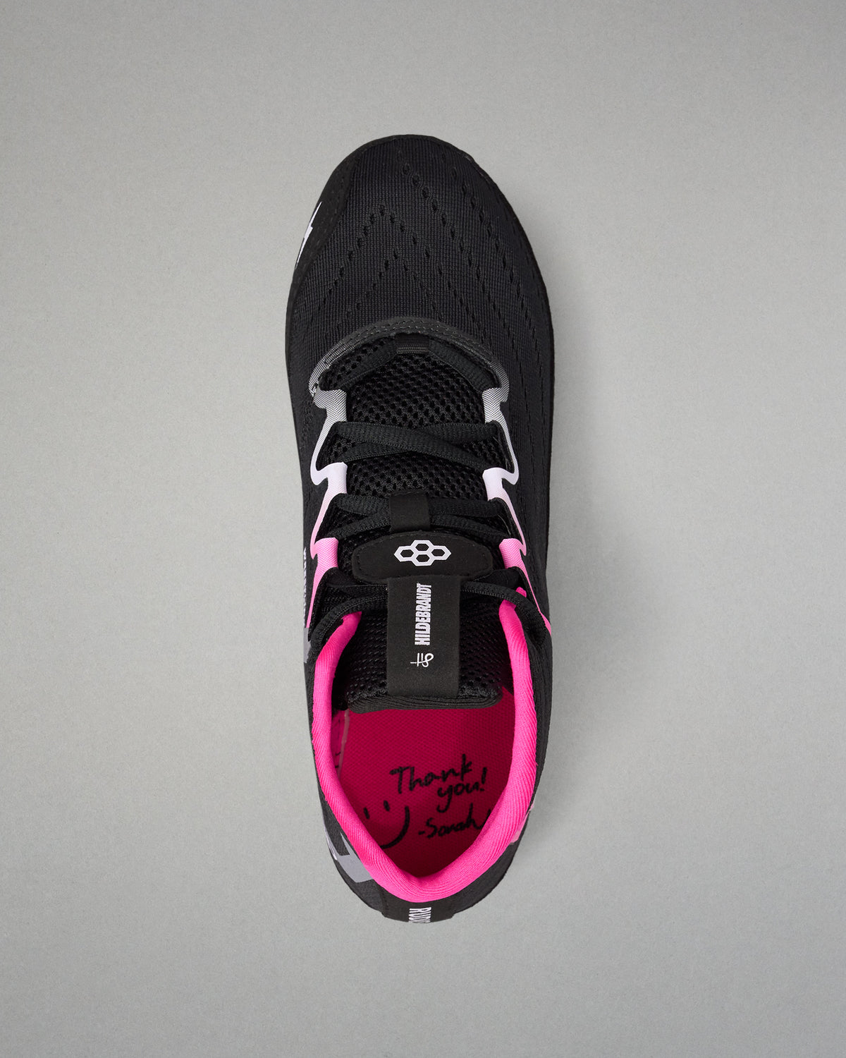 A black athletic wrestling shoe with vibrant pink accents, featuring a black mesh upper, white and black laces, and a bright pink inner lining with 'Thank you! So much' written on the footbed, shown from a top-down view on a neutral gray background.
