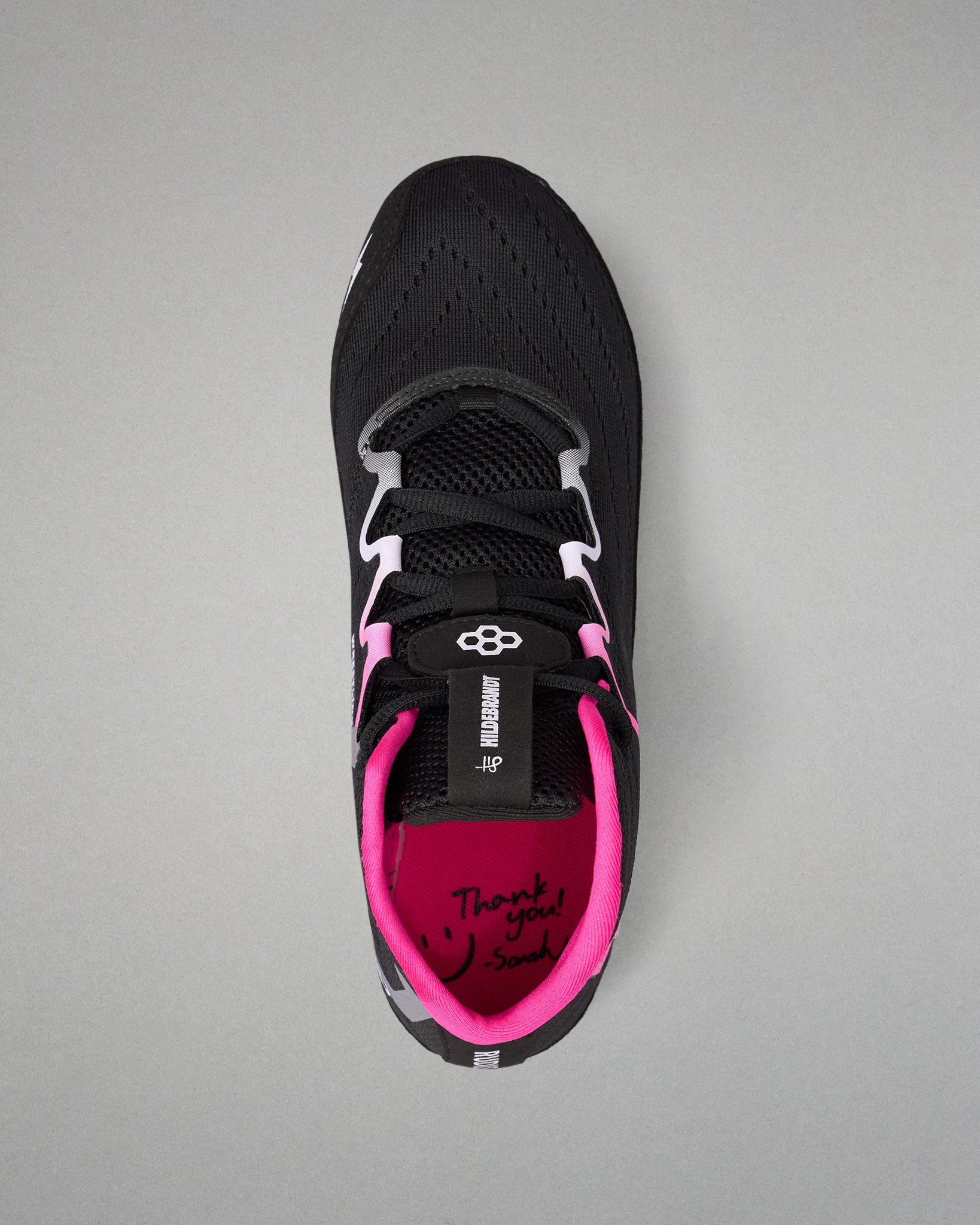 A black athletic wrestling shoe with vibrant pink accents, featuring a black mesh upper, white and black laces, and a bright pink inner lining with 'Thank you! So much' written on the footbed, shown from a top-down view on a neutral gray background.