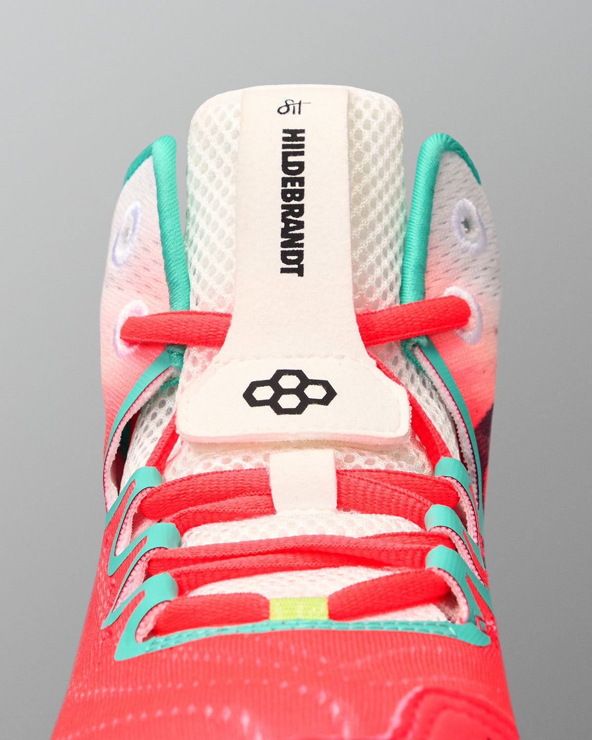 Close-up of the RUDIS Hildebrandt 2.0 Women’s Wrestling Shoe tongue with Hildebrandt branding, RUDIS logo, coral laces, and teal supports.