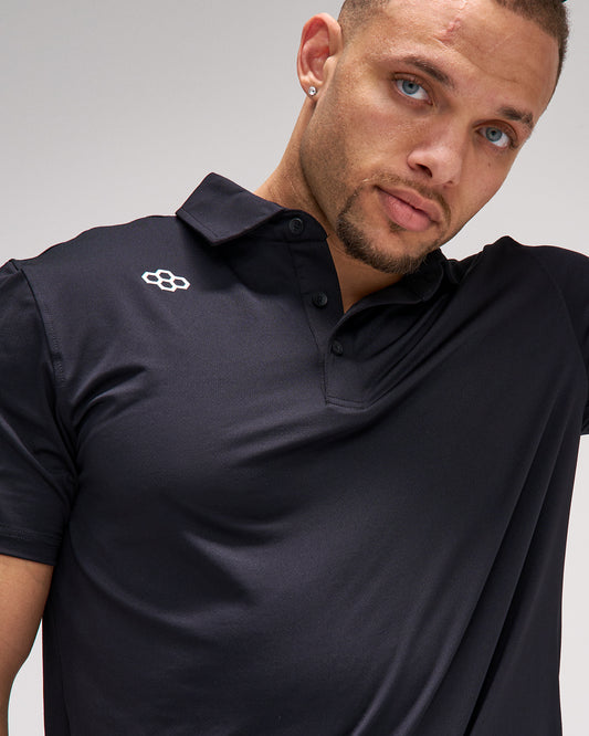 Man wearing a black polo shirt with a logo on a gray background