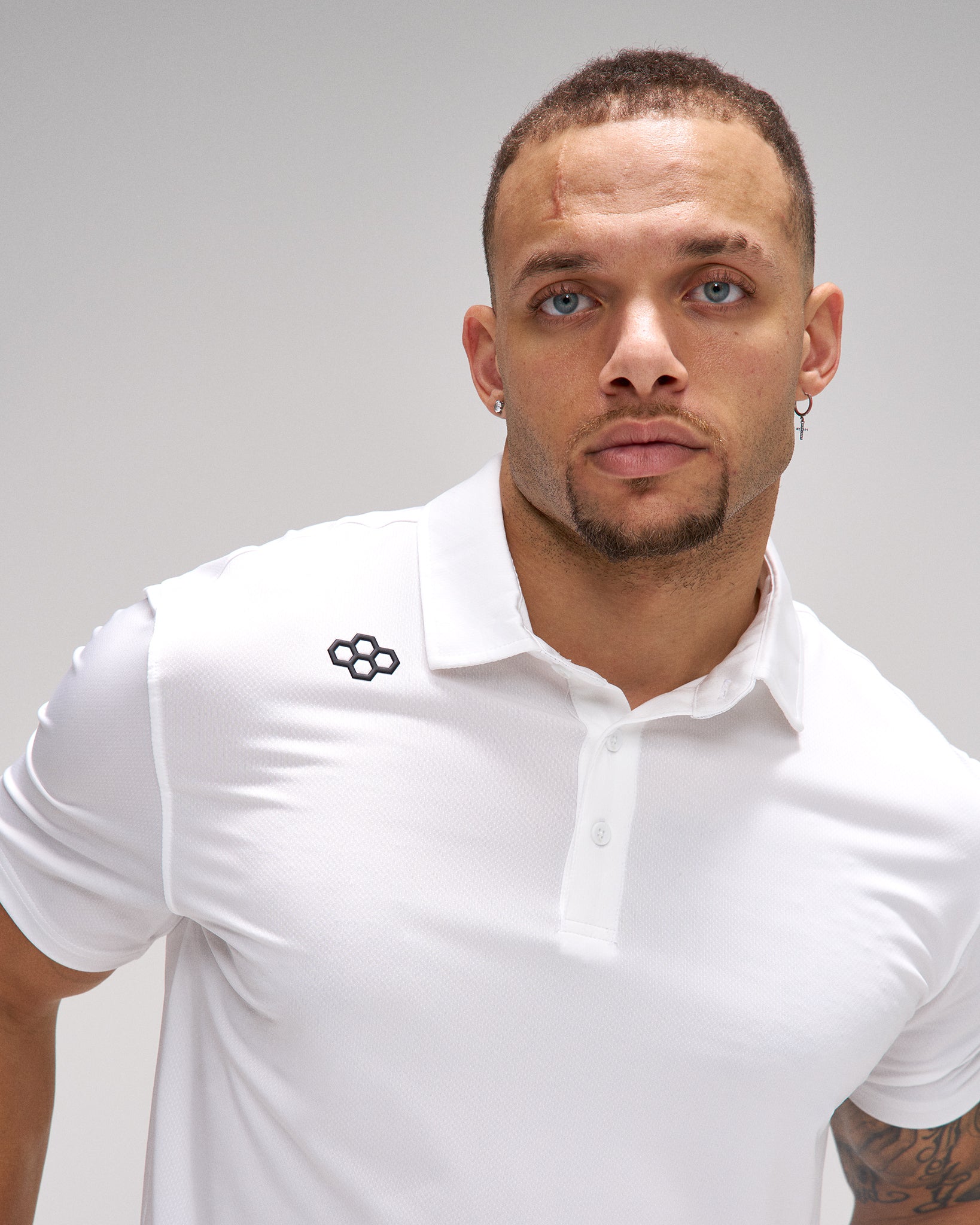 Man wearing a white polo shirt with a logo on a gray background