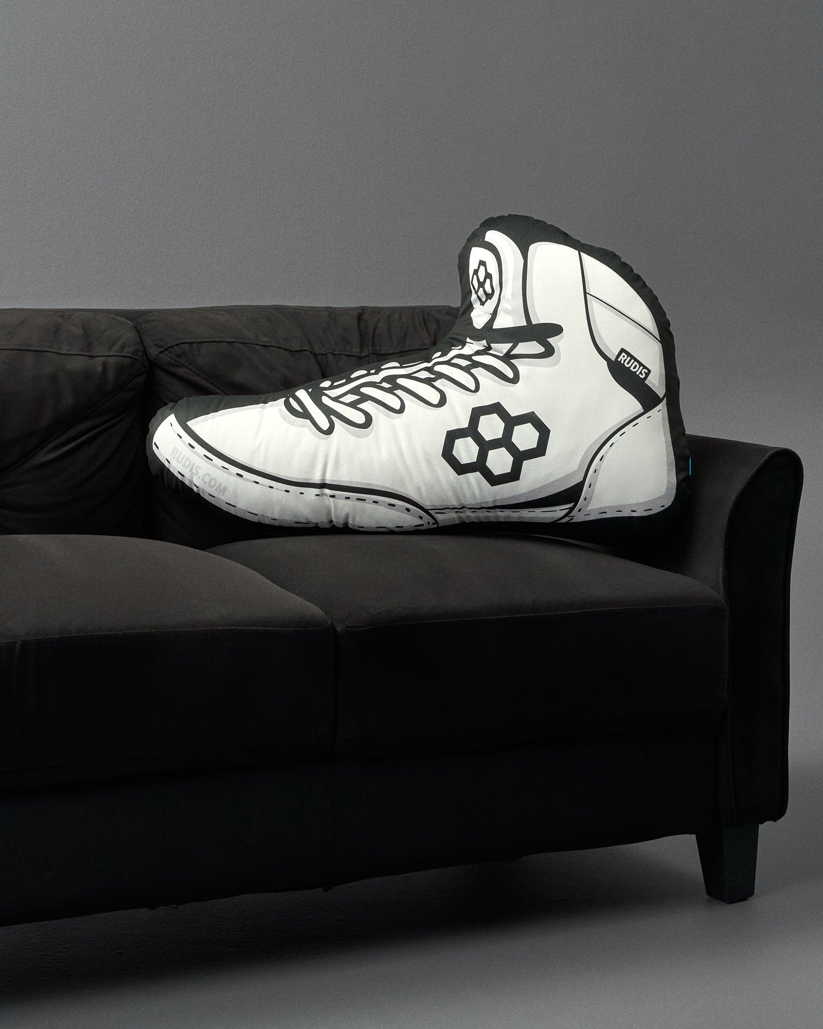 White high-top sneaker-shaped pillow on a black couch against a gray background