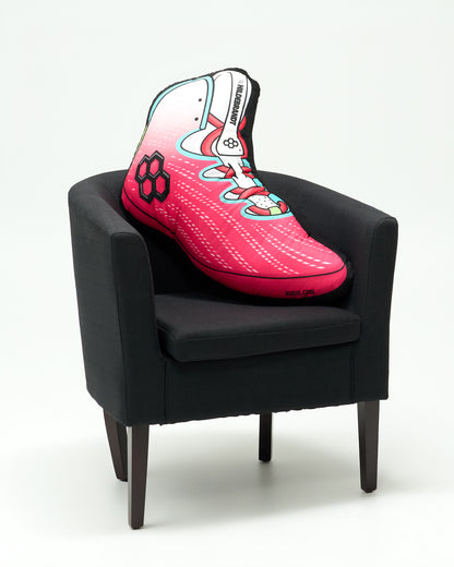 A pink and white high-top soccer cleat cushion styled on a black armchair against a clean white background.
