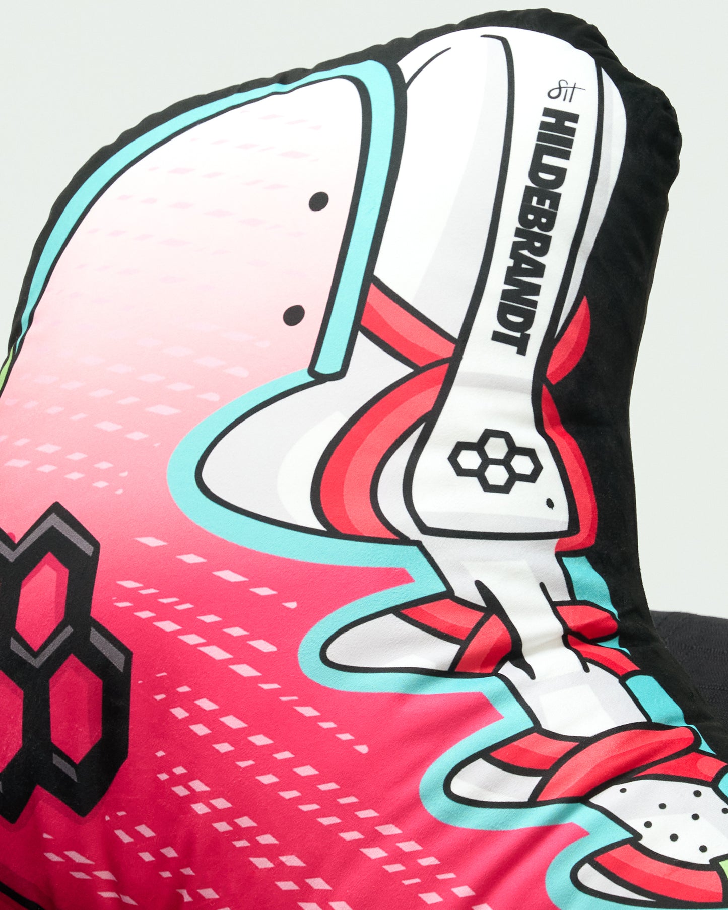 A close-up of a decorative cushion or pillow featuring a stylized soccer cleat design in pink, white, red, and light blue, with the text 'HILDEBRANDT' printed vertically on the side.