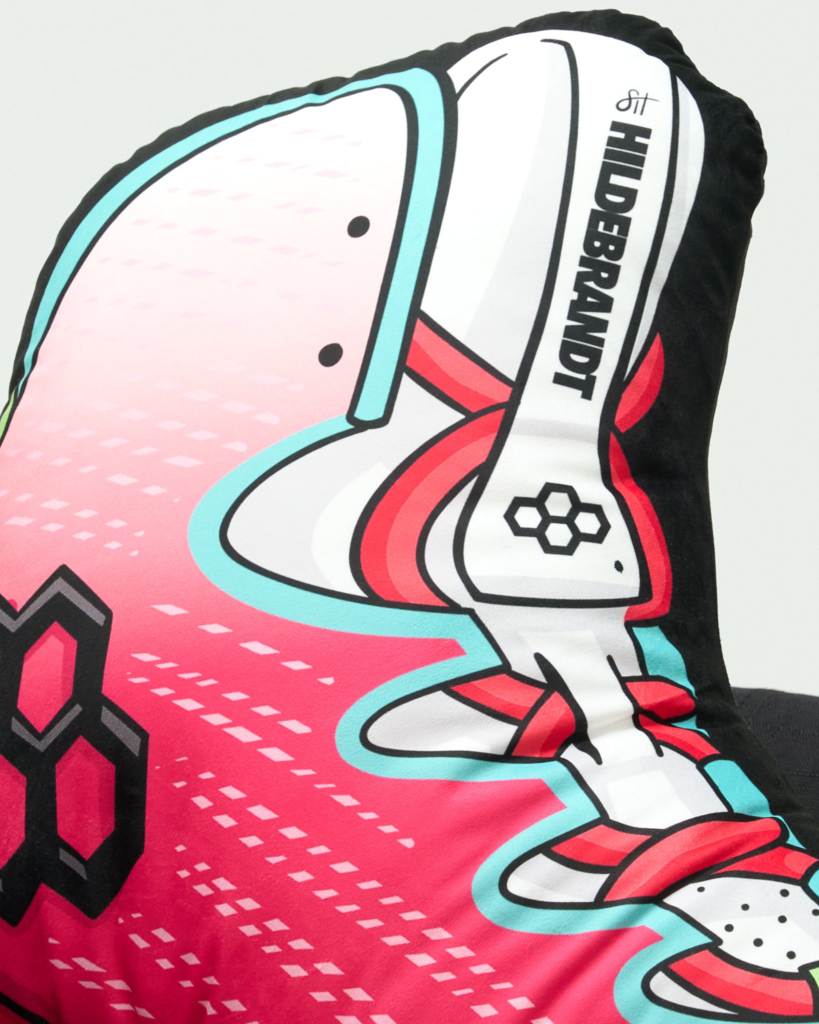 A close-up of a decorative cushion or pillow featuring a stylized soccer cleat design in pink, white, red, and light blue, with the text 'HILDEBRANDT' printed vertically on the side.