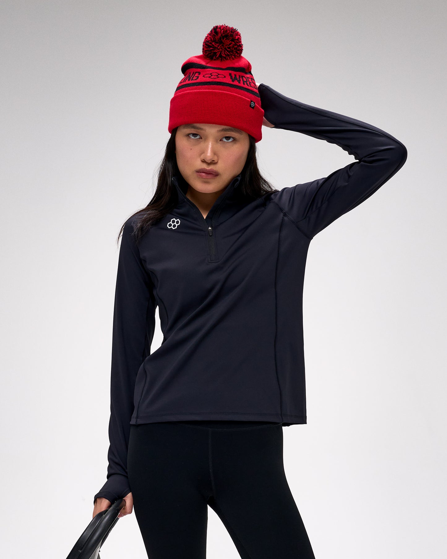 Person wearing a black jacket and red beanie with a logo on a light gray background