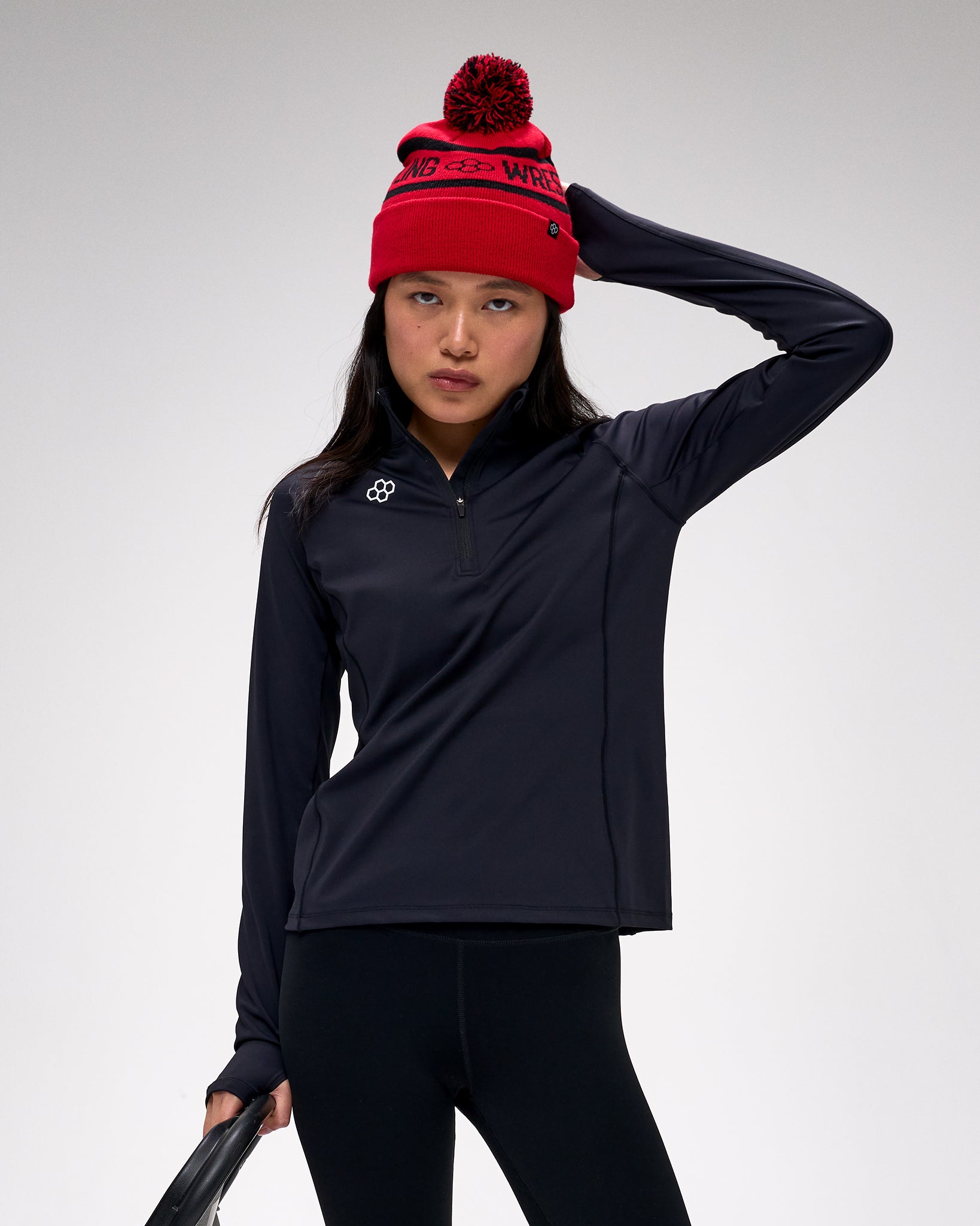 Person wearing a black jacket and red beanie with a logo on a light gray background