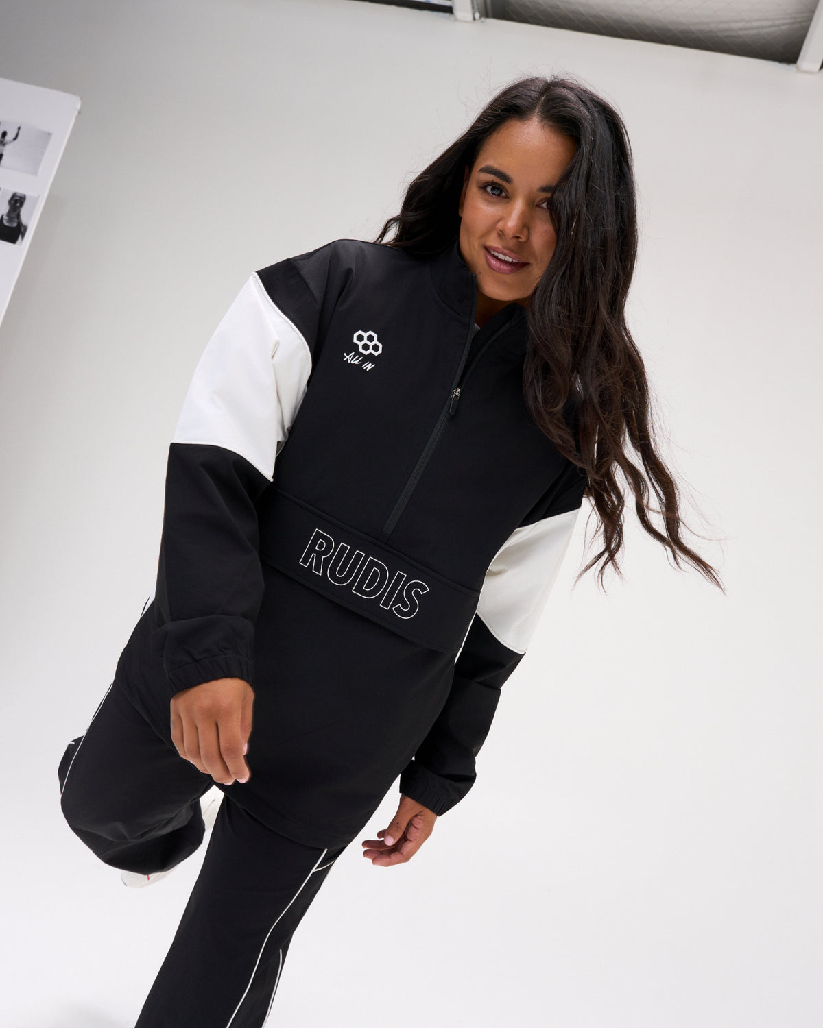 A woman modeling a black and white color-blocked athletic jacket with 'RUDIS' printed on the front, set against a clean white studio background.