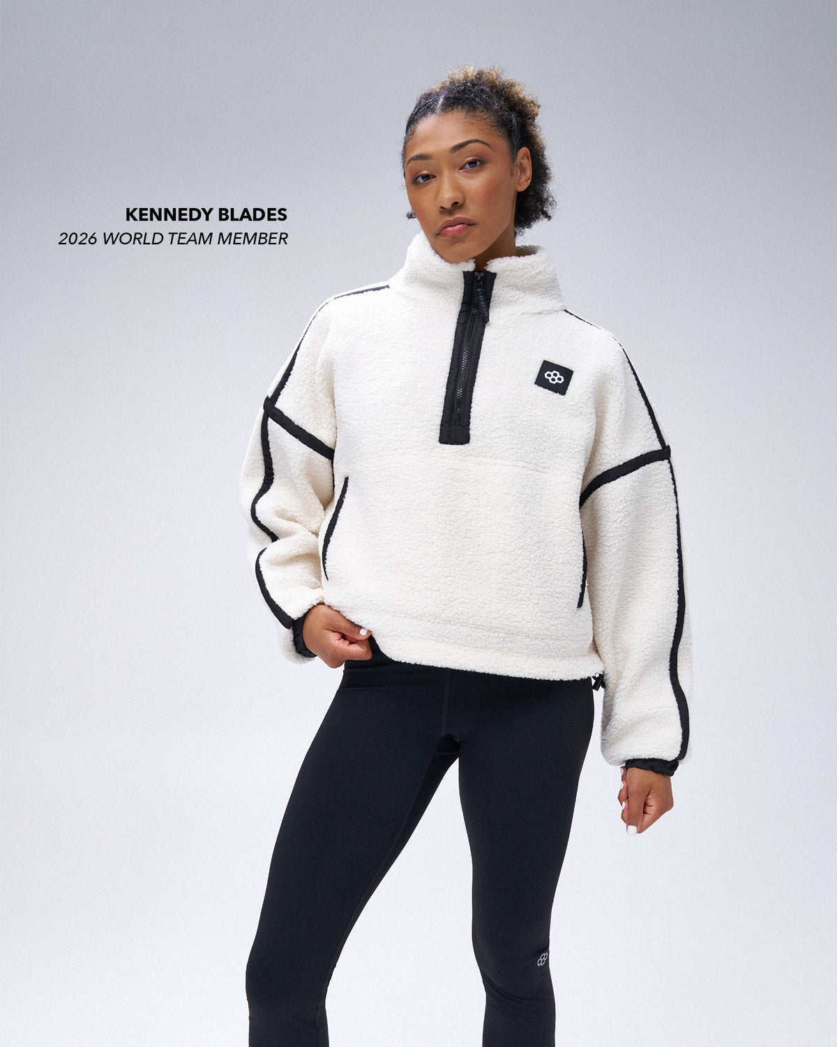 RUDIS athlete Kennedy Blades wearing a white women's sherpa quarter-zip pullover with black contrast stitching, a high collar, black zipper, and RUDIS chest logo, paired with black leggings.