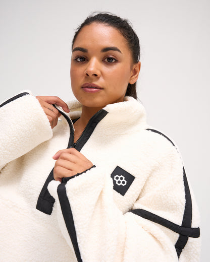 Close-up of a model wearing the RUDIS Women's Sherpa Half Zip in White/Black, featuring plush white fleece, black zipper trim, a stand collar and RUDIS chest logo.